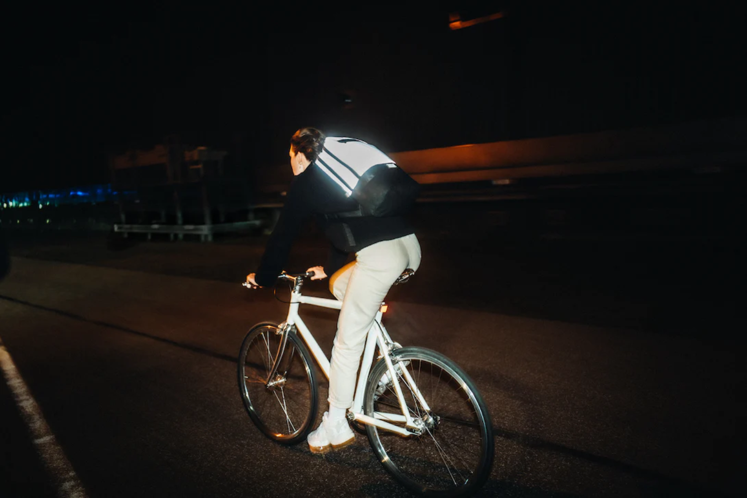 Fahrradfahrer bei Nacht mit leuchtendem Rucksack auf dunkler Straße