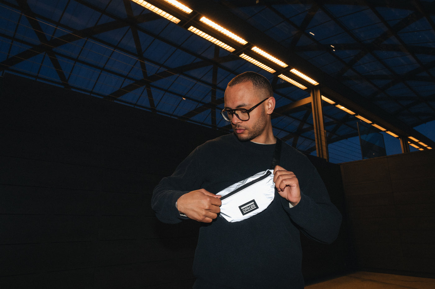 Mann mit schwarzer Brille trägt reflektierende weiße Bauchtasche von OAK25 über der Schulter