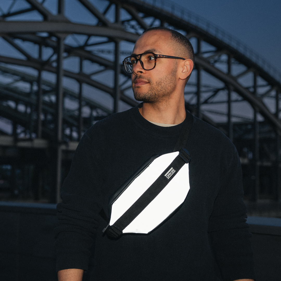 Mann trägt reflektierende schwarze Bauchtasche diagonal über der Brust vor einer Brücke bei Nacht