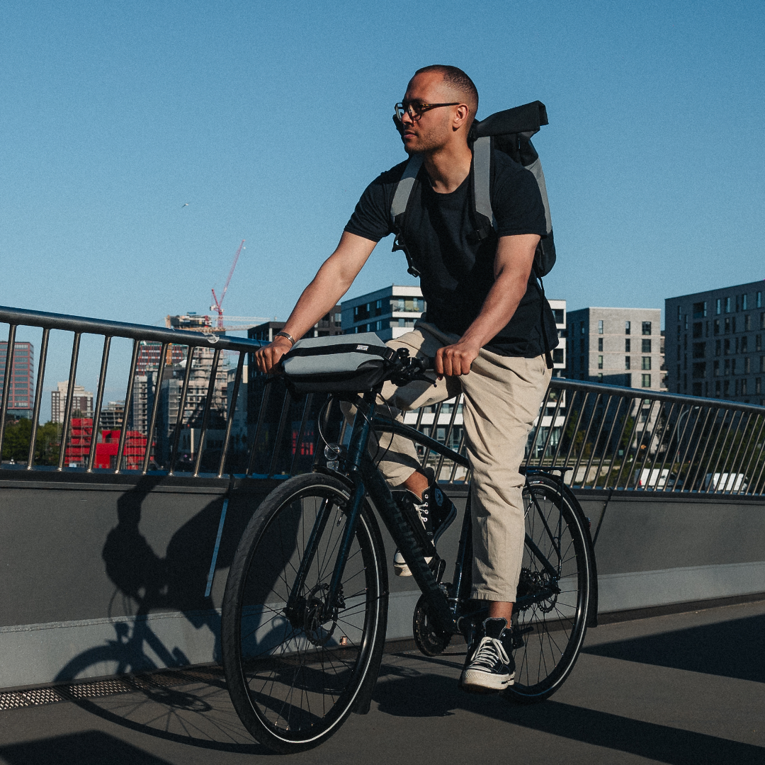 Mann auf schwarzem Fahrrad mit schwarzer reflektierender Fahrradtasche am Lenker auf Brücke