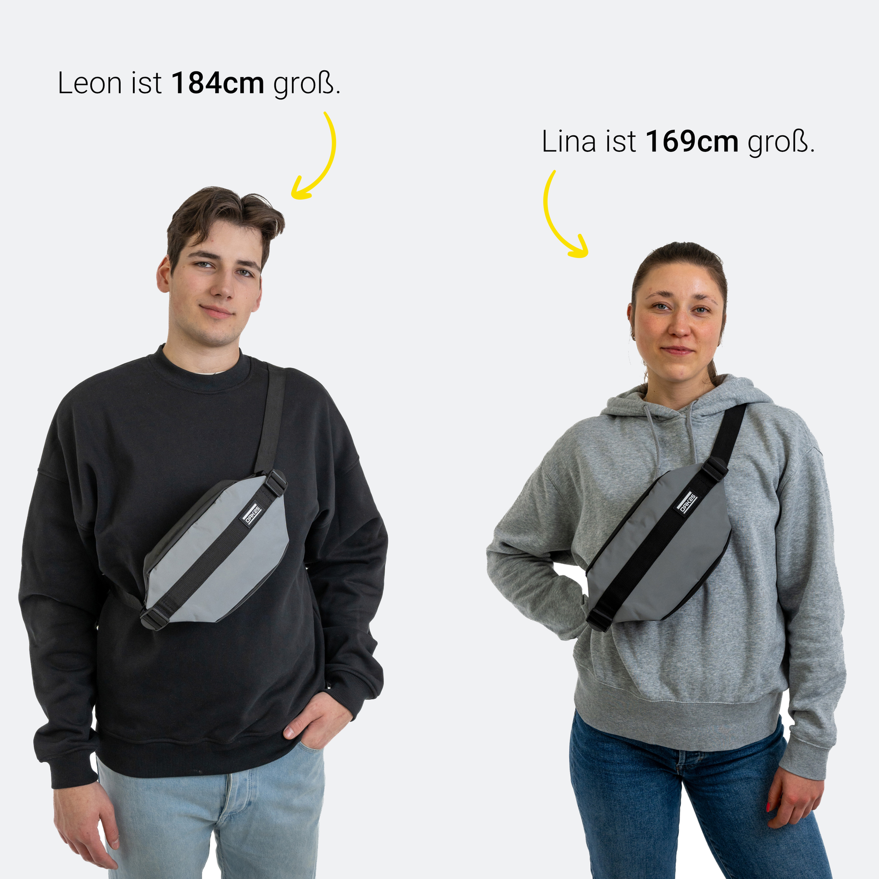 Zwei Personen mit unterschiedlich großen schwarzen Bauchtaschen, Leon ist 184 cm und trägt eine schwarze Bauchtasche quer über der Brust, Lina ist 169 cm und trägt die gleiche Tasche