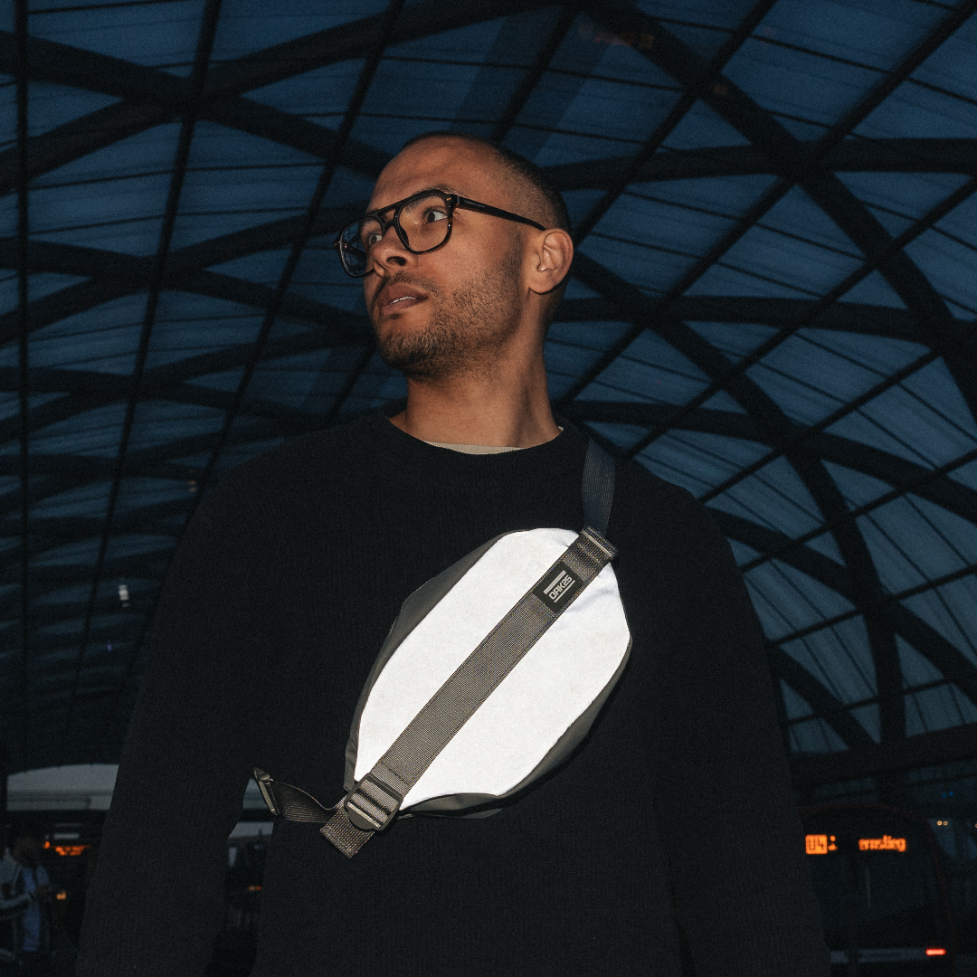 Mann mit Brille trägt reflektierende Bauchtasche von OAK25 über schwarzem Pullover