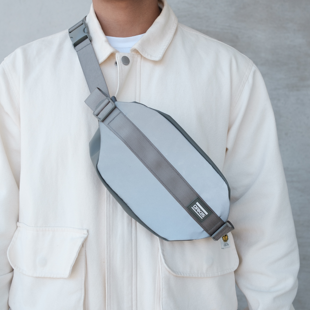 Reflektierende, hellgraue OAK25 Crossbody-Tasche aus robustem Material, getragen über der Brust