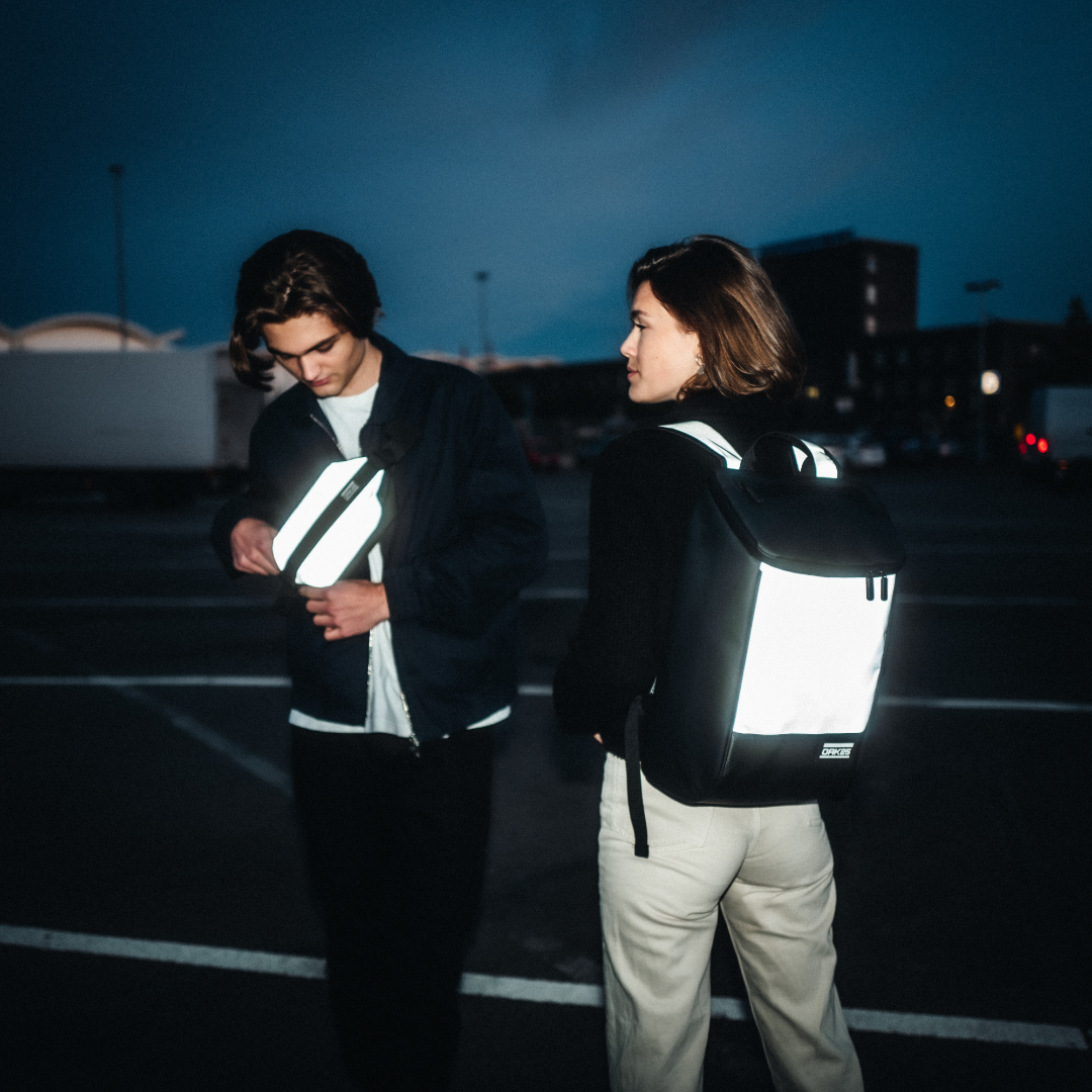 Junge Frau mit reflektierendem schwarzen Rucksack und junger Mann mit reflektierender schwarzen Bauchtasche bei Nacht