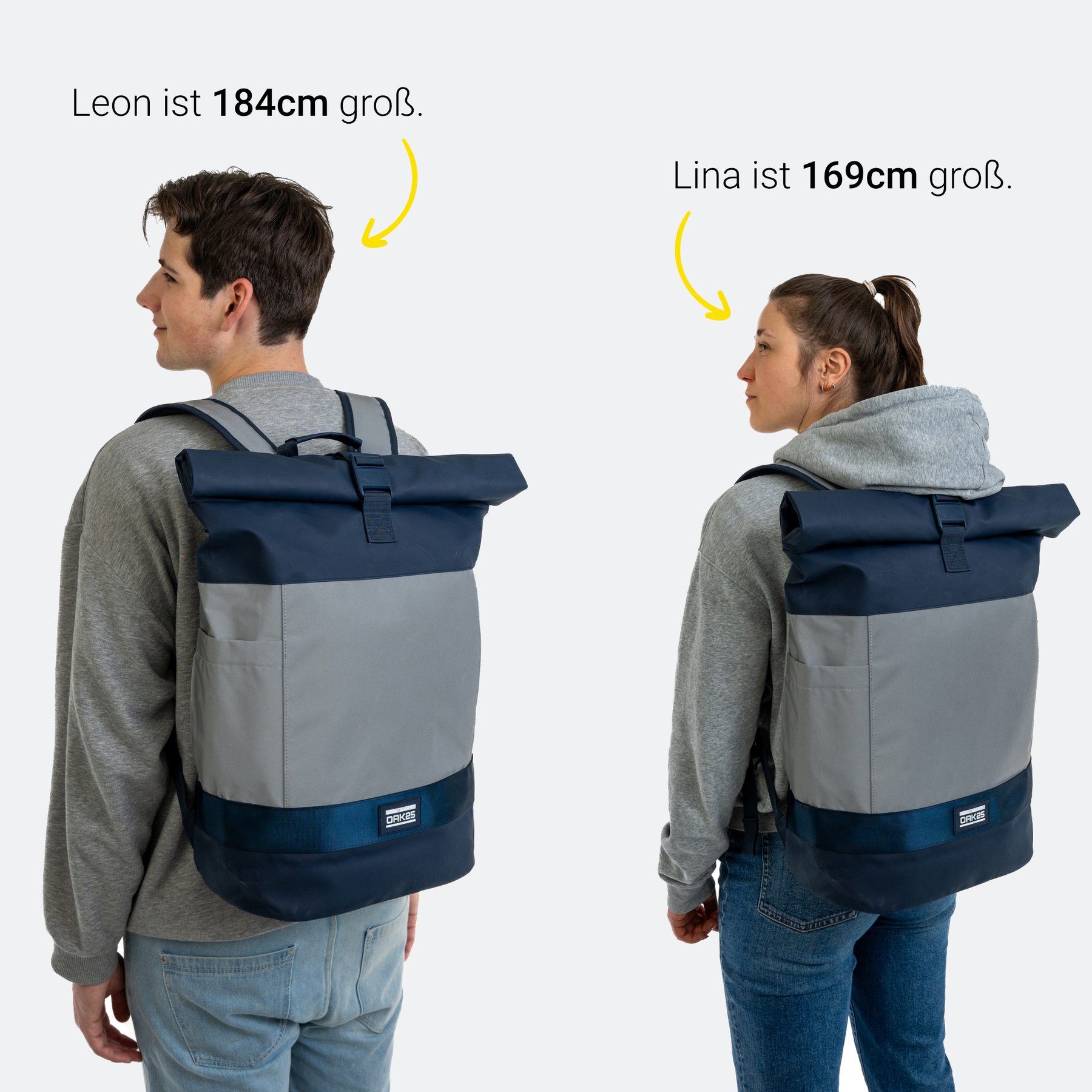 Zwei Personen mit grauzugem Kapuzenpullover tragen reflektierende Rolltop-Rucksäcke in Navy und Grau. Links Leon, 184 cm groß, rechts Lina, 169 cm groß.