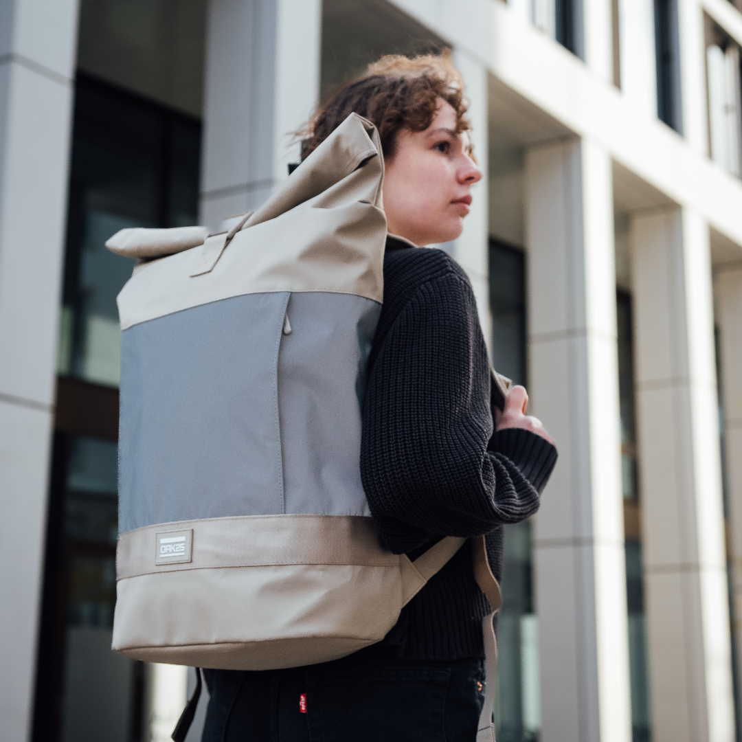 Unisex Fahrradrucksack OAK25 Commute Rolltop in Sandfarbe mit reflektierendem grauem Mittelteil, getragen von einer Person mit schwarzem Pullover