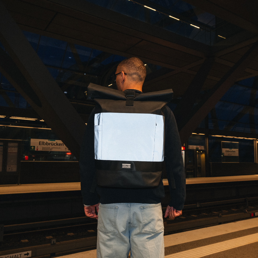 Mann mit schwarzem OAK25 Rolltop Fahrradrucksack mit reflektierender Fläche am Bahnhof Elbbrücken