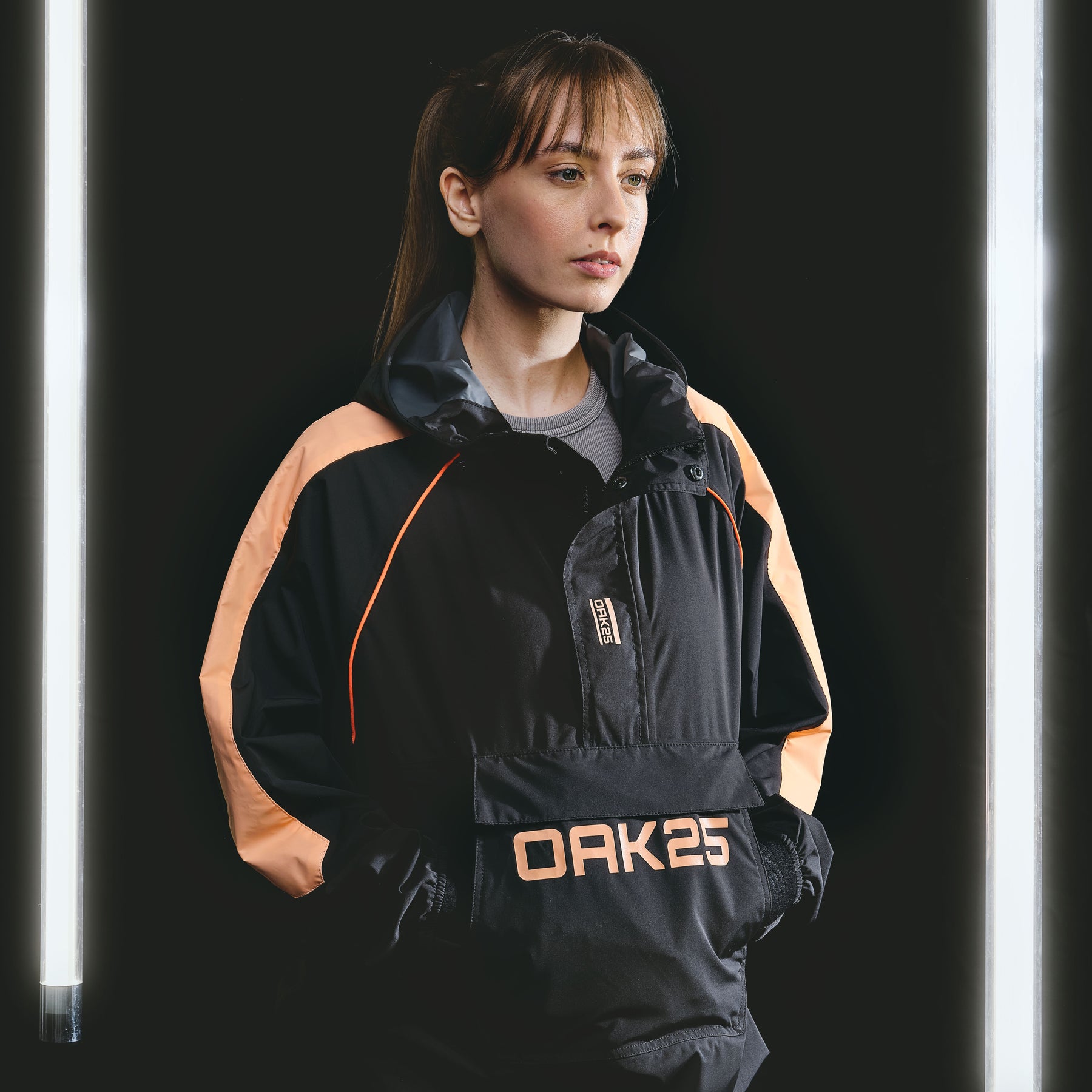 Frau mit schwarzem und pfirsichfarbenem OAK25 Windbreaker mit Kapuze und Logo vorne