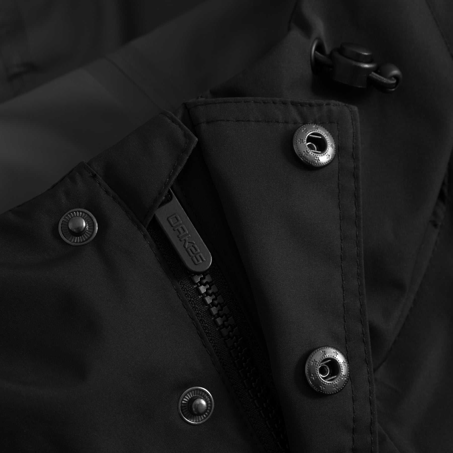 Nahaufnahme eines schwarzen Windbreakers mit OAK25 Reißverschluss und Druckknöpfen mit verschweißten Nähten