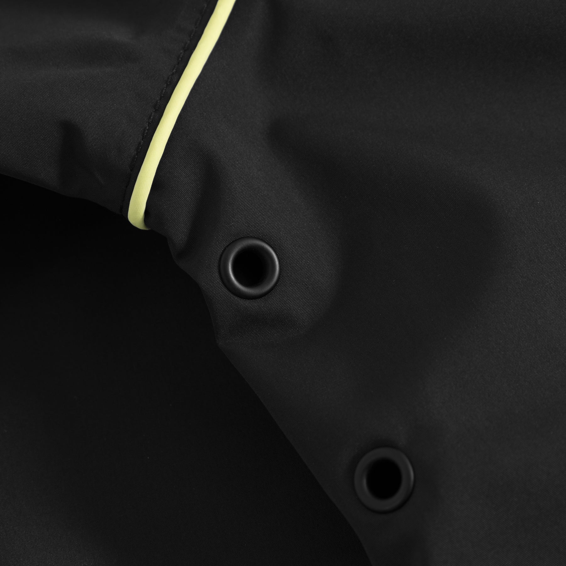 Nahaufnahme von schwarzem atmungsaktivem Windbreaker-Stoff mit zwei schwarzen Ösen und gelbem Paspel
