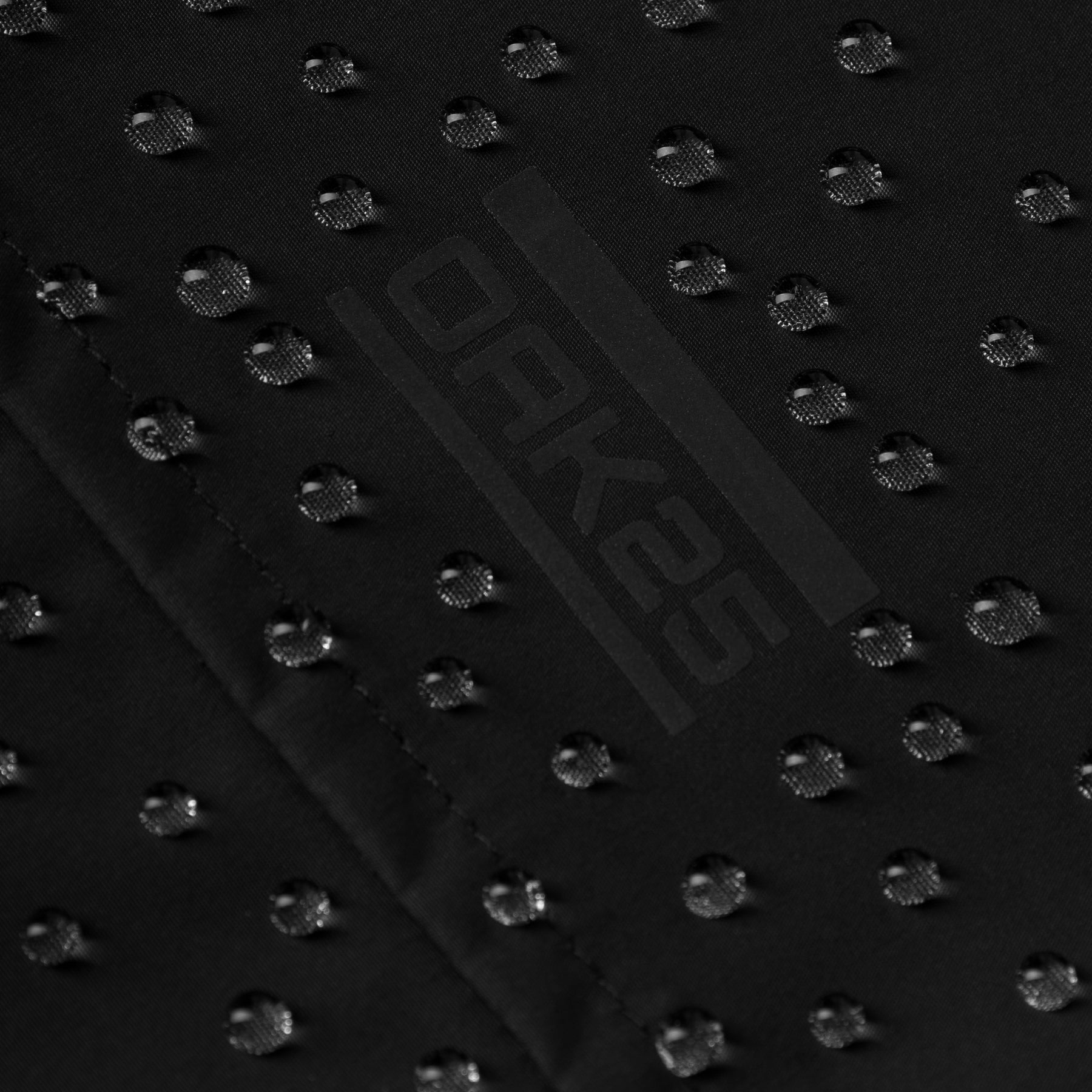 Schwarzes wasserabweisendes Stoffdetail mit Wasserperlen und OAK25 Logo