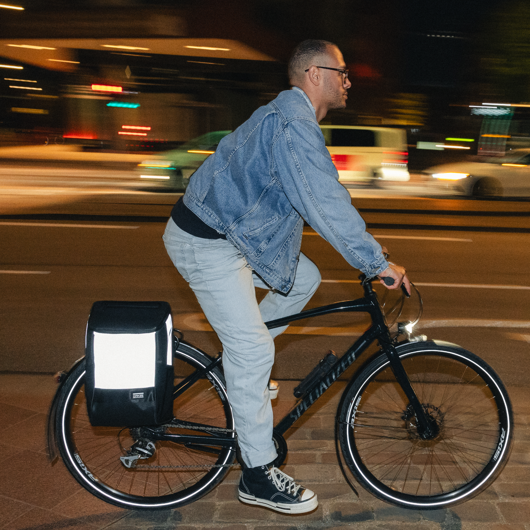 Mann auf schwarzem Fahrrad mit reflektierender schwarzer Fahrradtasche auf Gepäckträger bei Nacht
