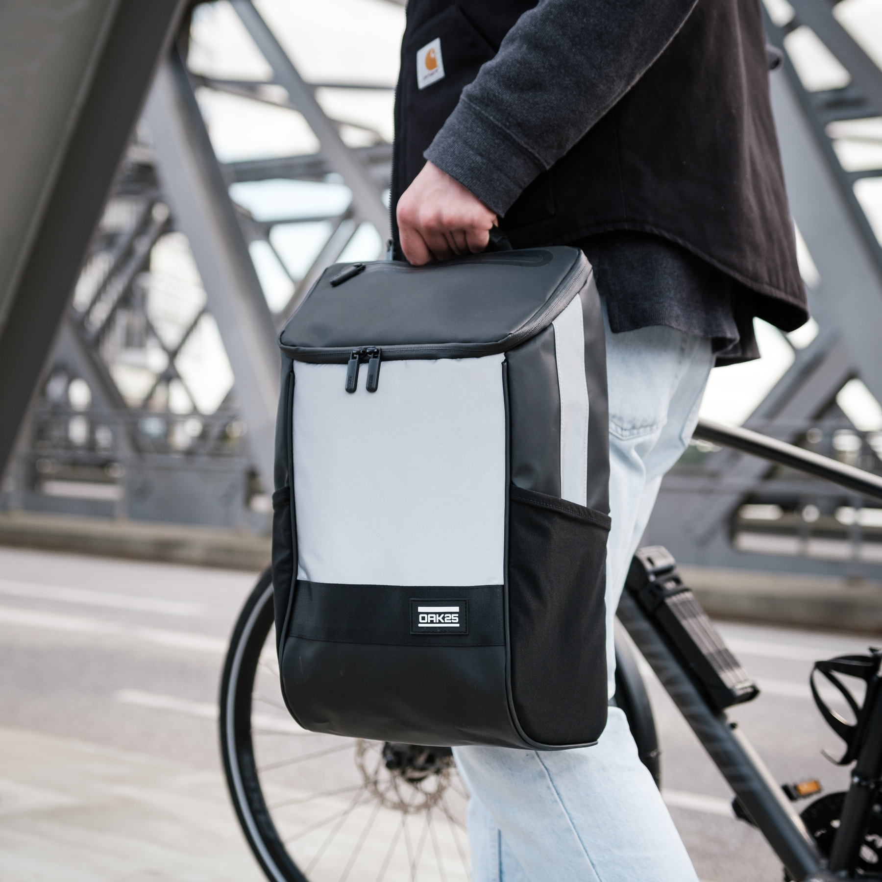 Schwarze und reflektierende Fahrradtasche OAK25 Daybag wird von Person neben Fahrrad gehalten