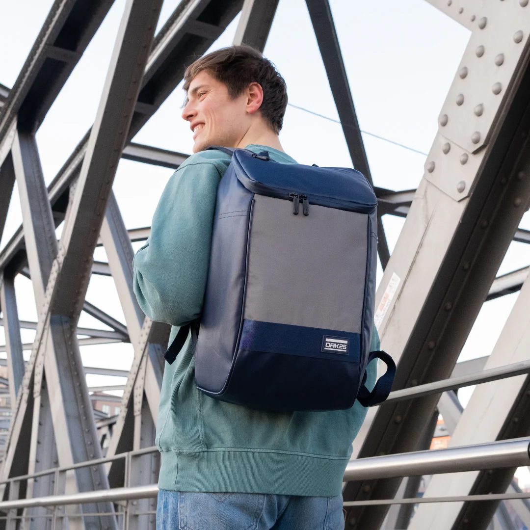 Junger Mann trägt rechteckigen OAK25 Daybag in navy mit reflektierendem grauem Vorderteil auf dem Rücken