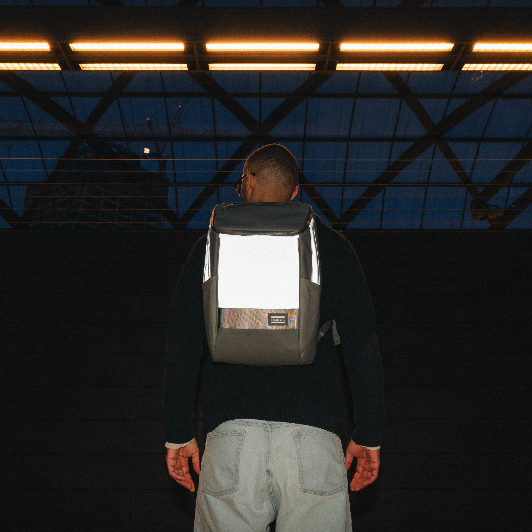 Rückenansicht eines Mannes mit schwarzem reflektierendem Rucksack bei Nacht unter beleuchtetem Dach