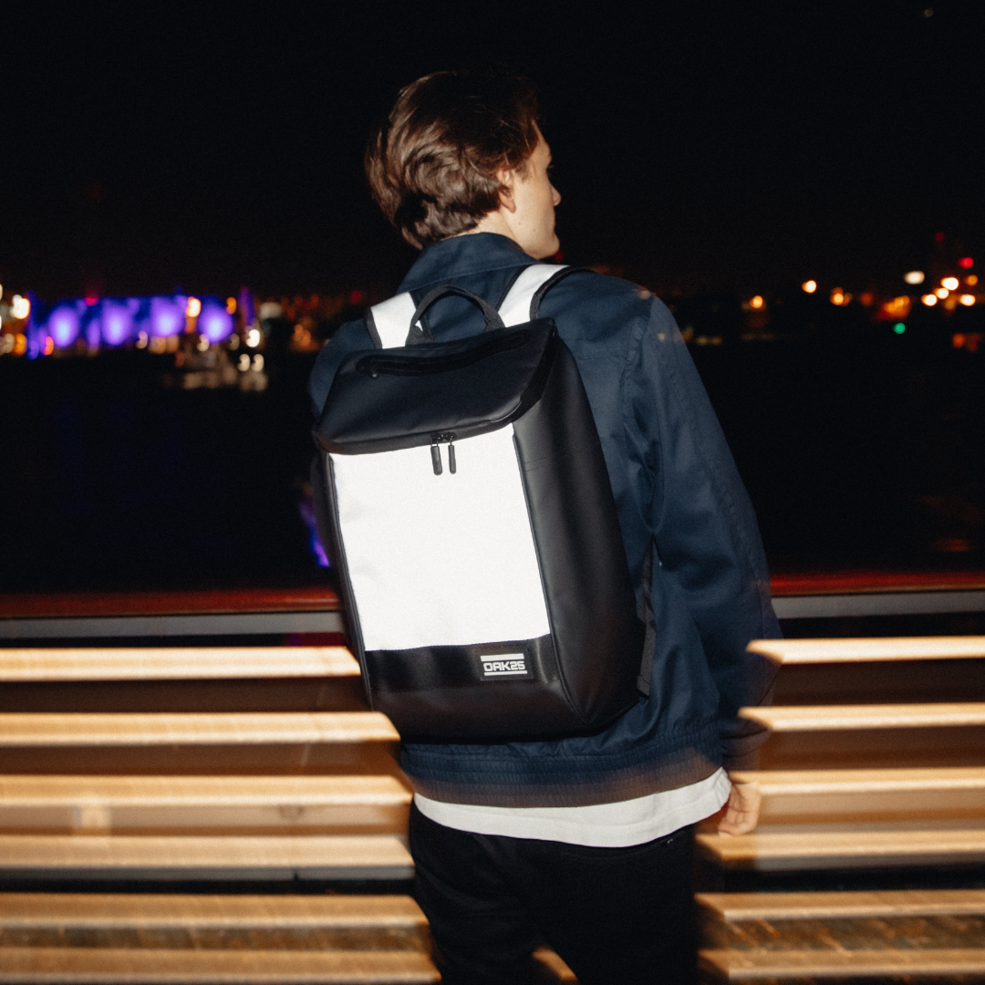 Person trägt schwarzen und weißen OAK25 Daybag-Rucksack mit reflektierendem Material bei Nacht