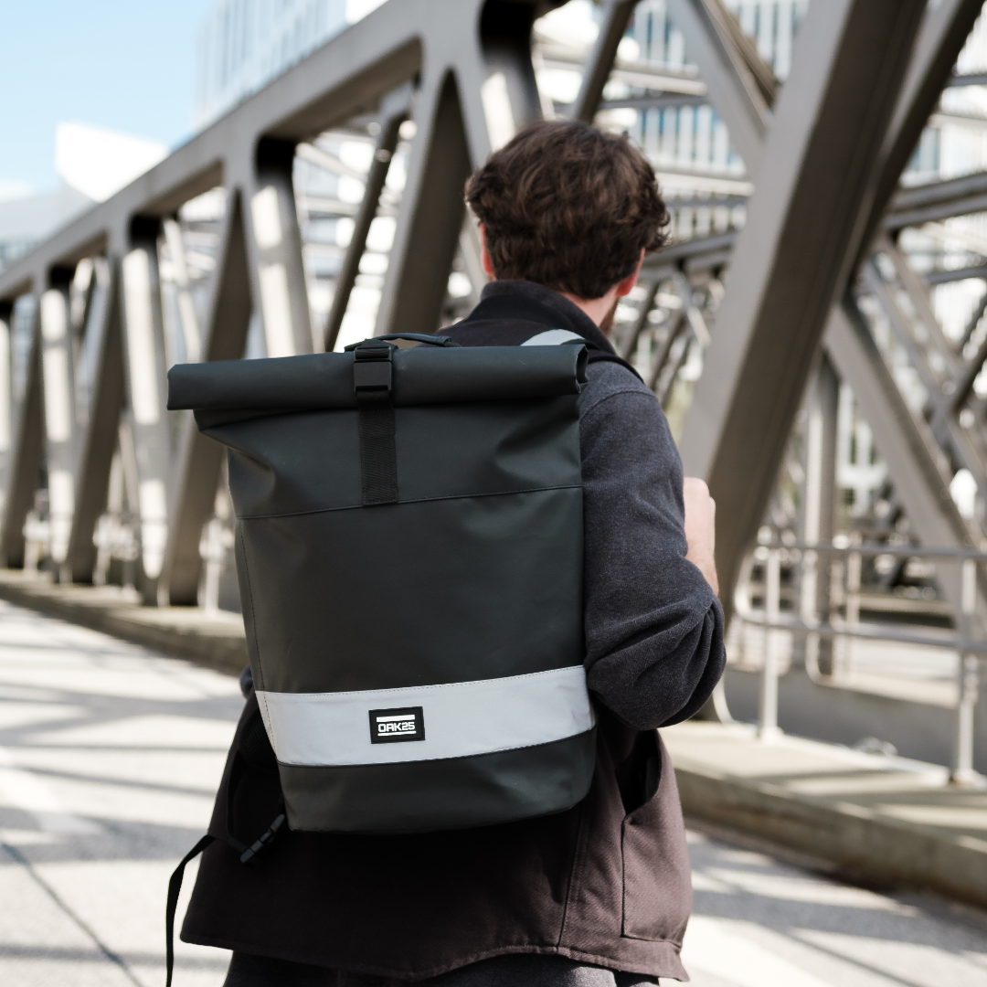 Mann trägt schwarzen OAK25 Rolltop Fahrrucksack mit reflektierendem Streifen auf dem Rücken