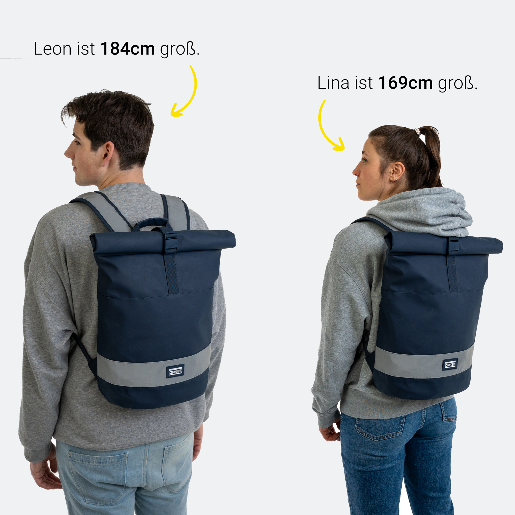 Junge und Mädchen tragen dunkelblaue OAK25 Rolltop-Rucksäcke mit reflektierendem Streifen, Größenangabe über ihren Köpfen