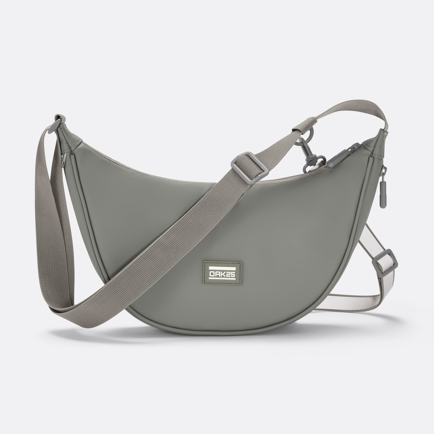 Salbei-farbene Halbmondtasche von OAK25 mit verstellbarem Gurt und Logo-Label auf der Vorderseite