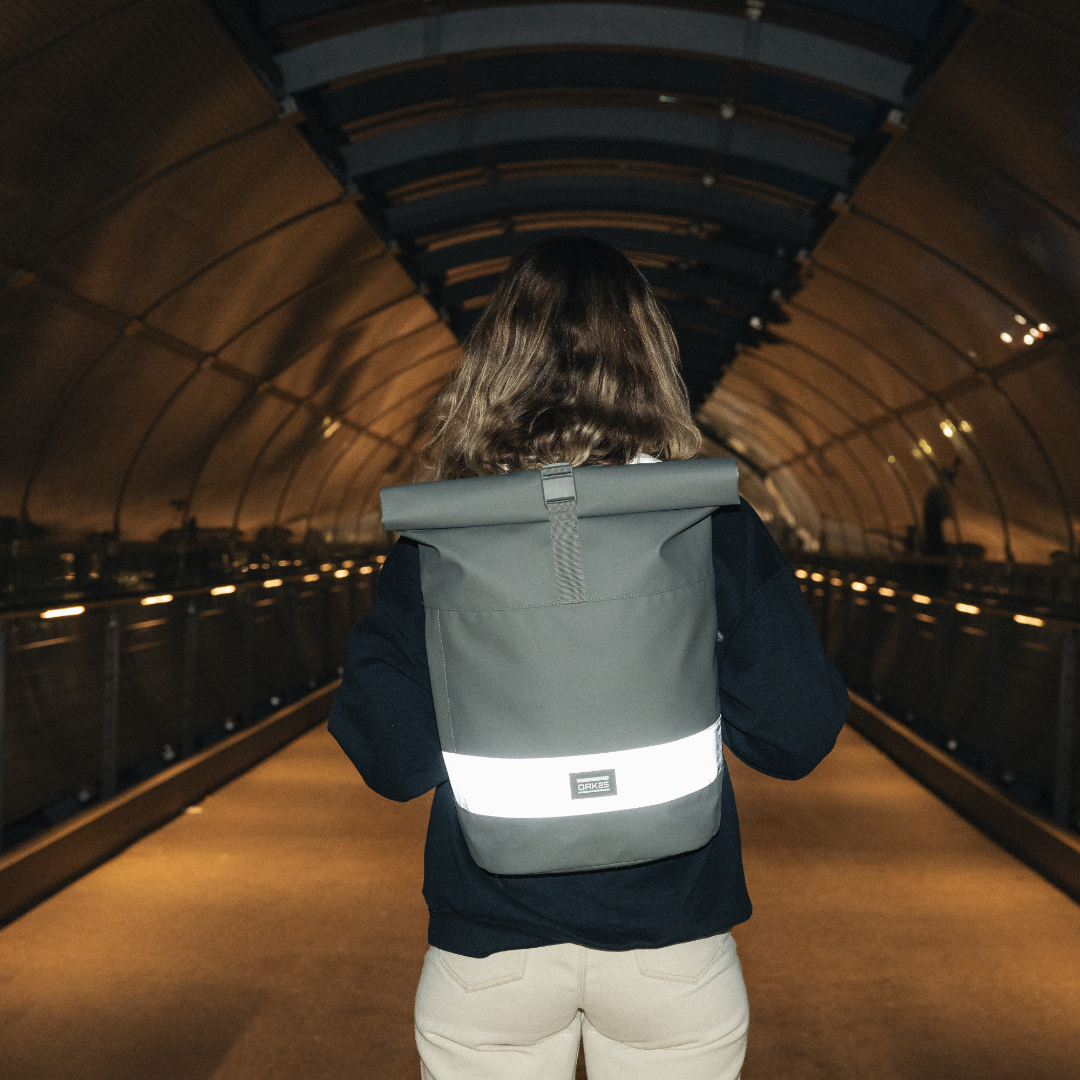 Person von hinten mit salbeigrünem Rolltop-Rucksack mit reflektierendem Streifen an einem beleuchteten Fußgängertunnel