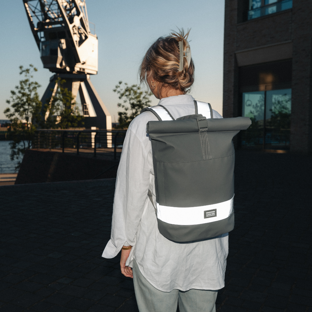 Person trägt reflektierenden Rolltop-Rucksack in Salbeigrün an einem Hafen bei Abendlicht