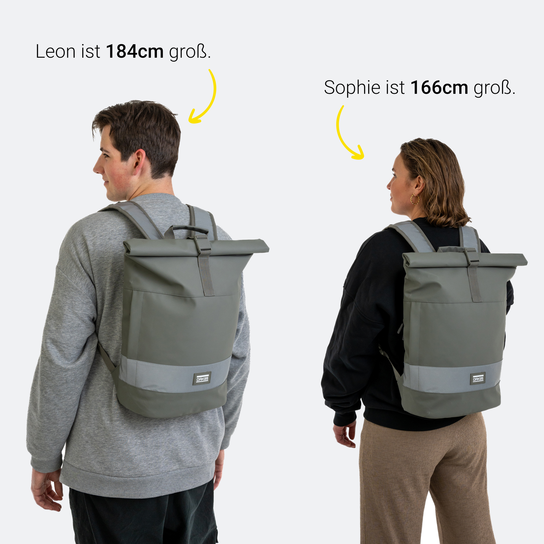Zwei Personen tragen einen salbeigrünen OAK25 Rolltop-Rucksack mit reflektierendem Streifen, Leon ist 184 cm und Sophie 166 cm groß