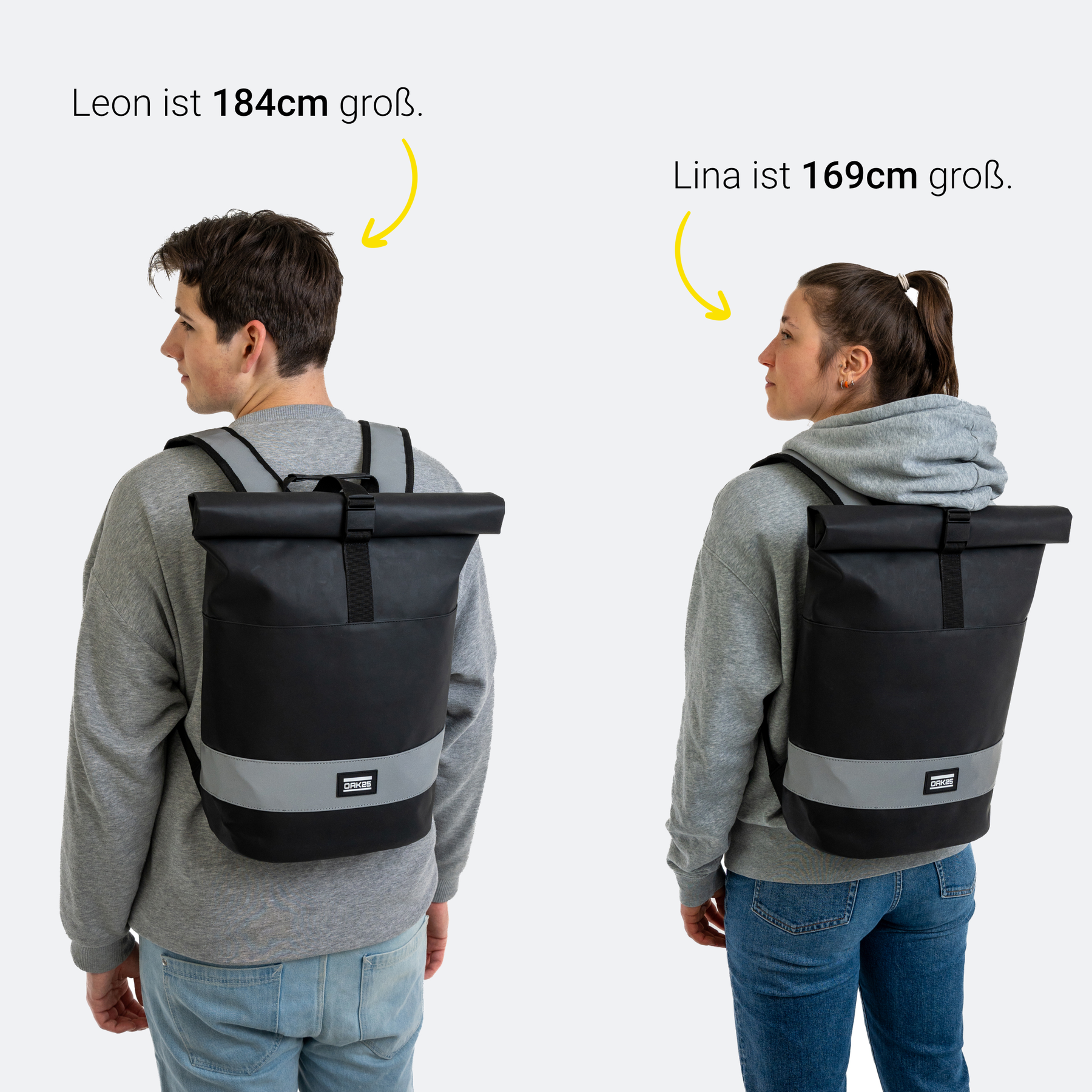 Zwei Personen tragen schwarze OAK25 Everyday Rolltop Rucksäcke mit reflektierendem Streifen, links Leon (184 cm), rechts Lina (169 cm).