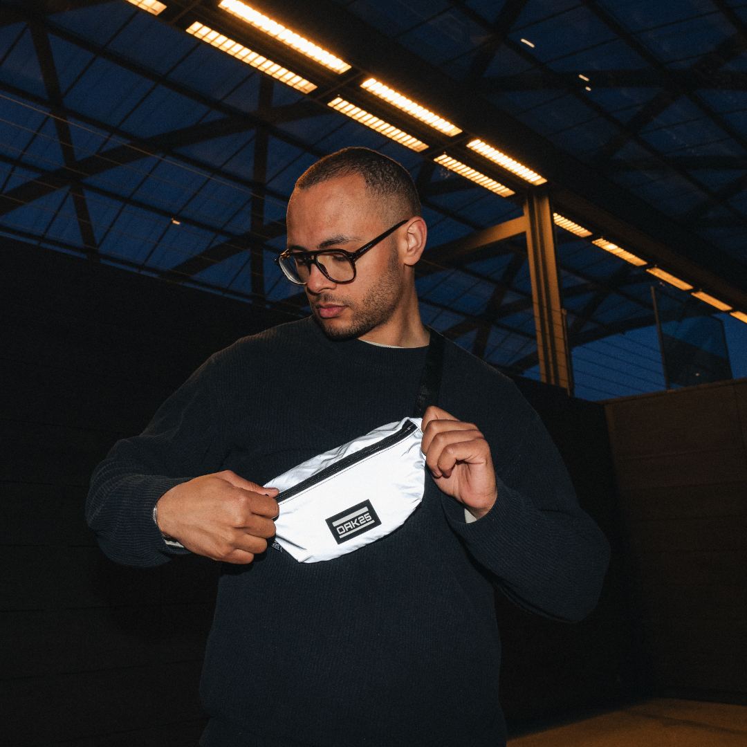 Mann trägt reflektierende OAK25 Everyday Sling Bauchtasche in Weiß über schwarzem Pullover