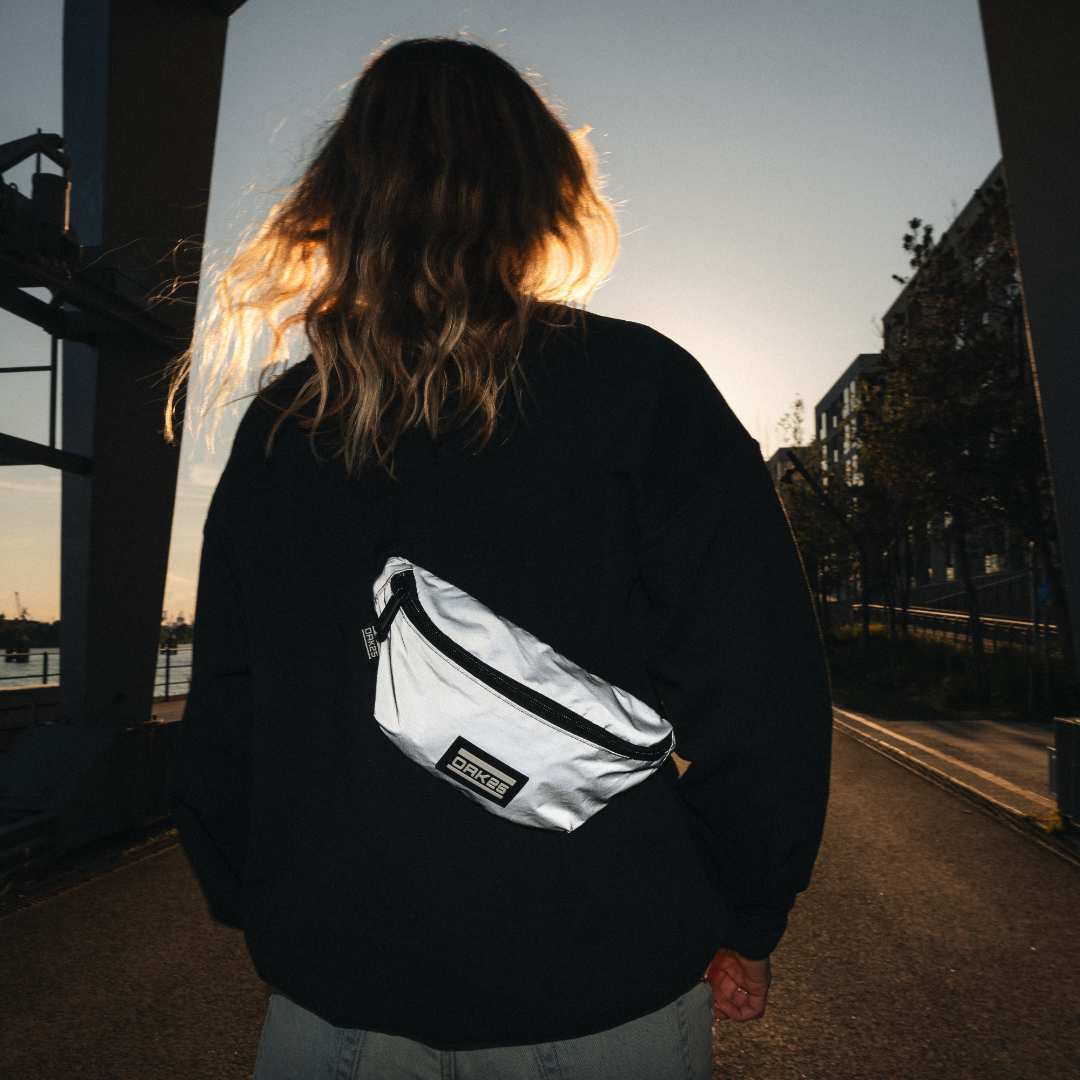 Person mit reflektierender grauer OAK25 Sling-Bauchtasche bei Sonnenuntergang, urbanes Umfeld