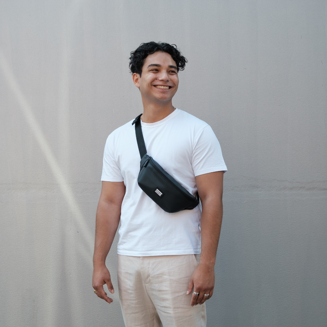 Mann in weißem T-Shirt und beiger Hose trägt schwarze Sling-Bauchtasche quer über der Brust
