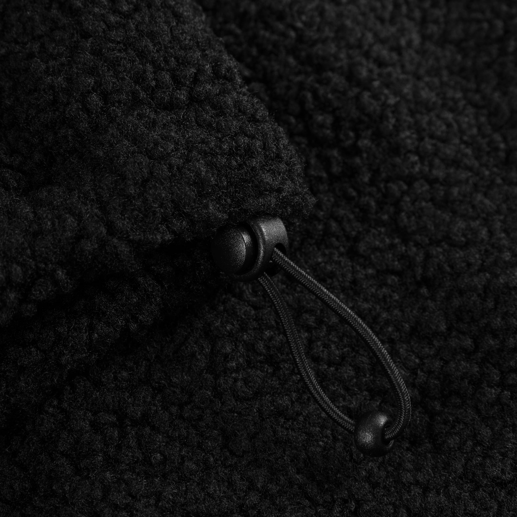 Schwarzer Kordelzug mit Stopper an einer Teddy-Jacke mit weichem, noppigem Material