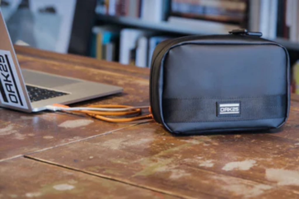 Schwarze OAK25 Tasche aus Leder neben einem geöffneten Laptop auf einem Holztisch