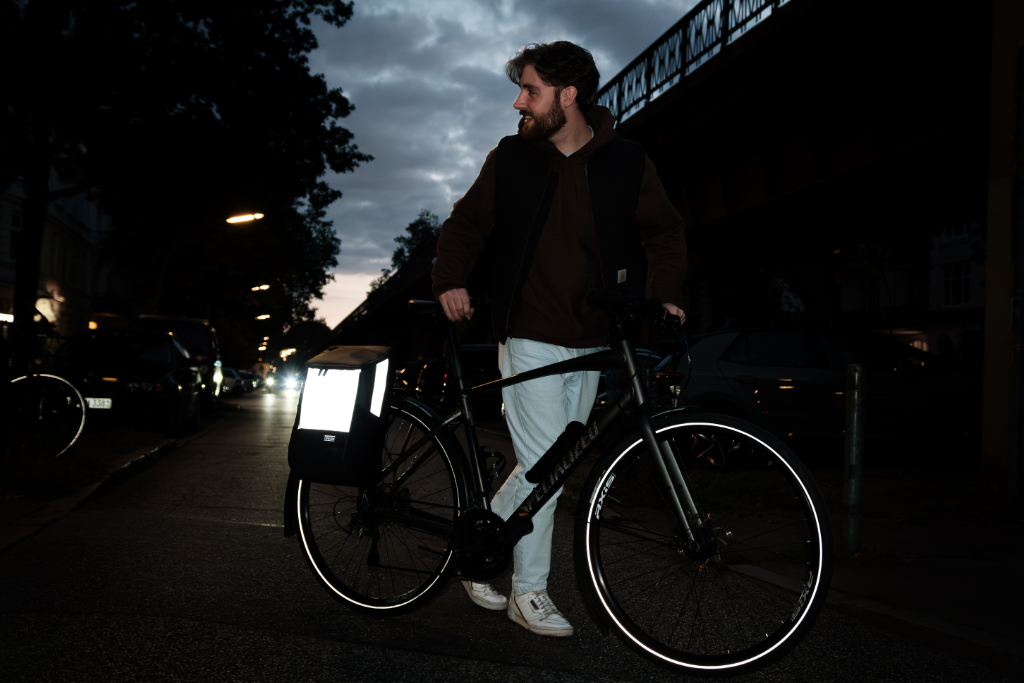 Mann steht nachts mit schwarzem Fahrrad und reflektierendem Fahrradtasche auf Straße