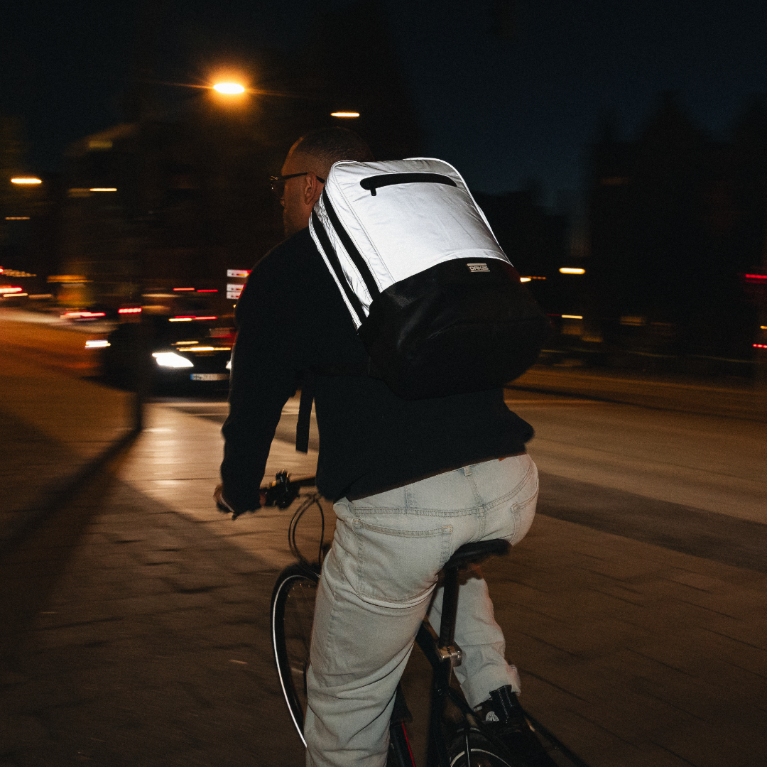 Person fährt nachts Fahrrad mit reflektierendem schwarz-weißem Rucksack