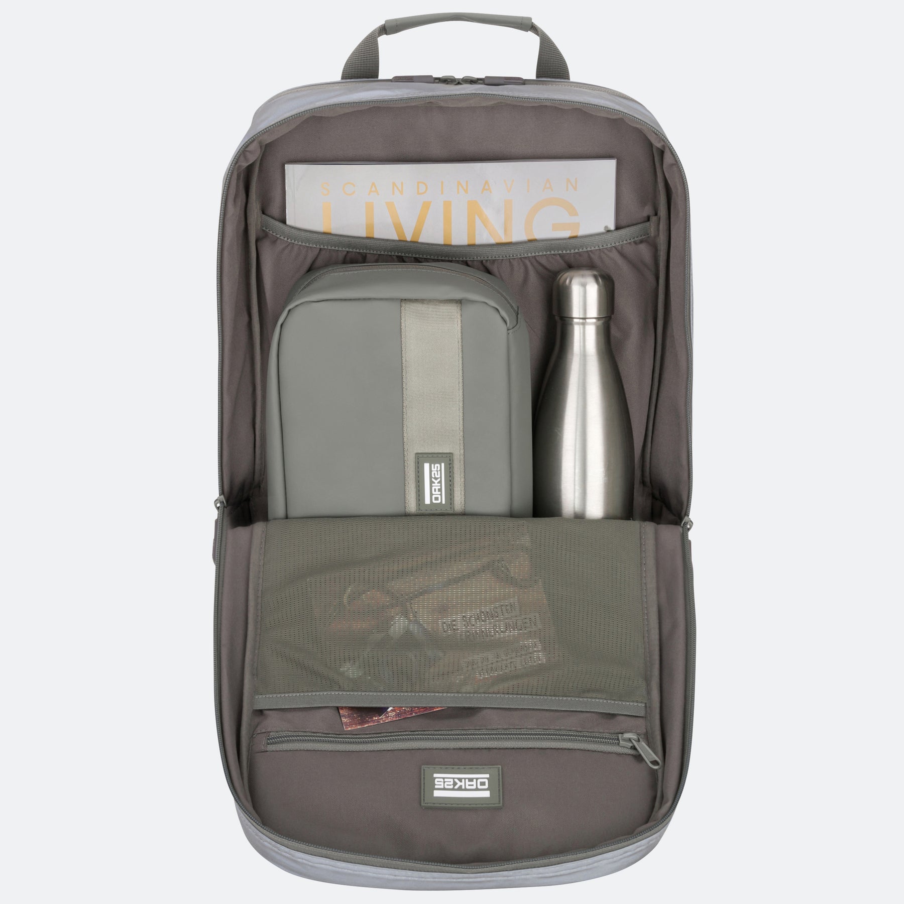 Geöffneter salbeigrüner Rucksack mit großem Hauptfach, Tasche, Metallflasche und Zeitschrift