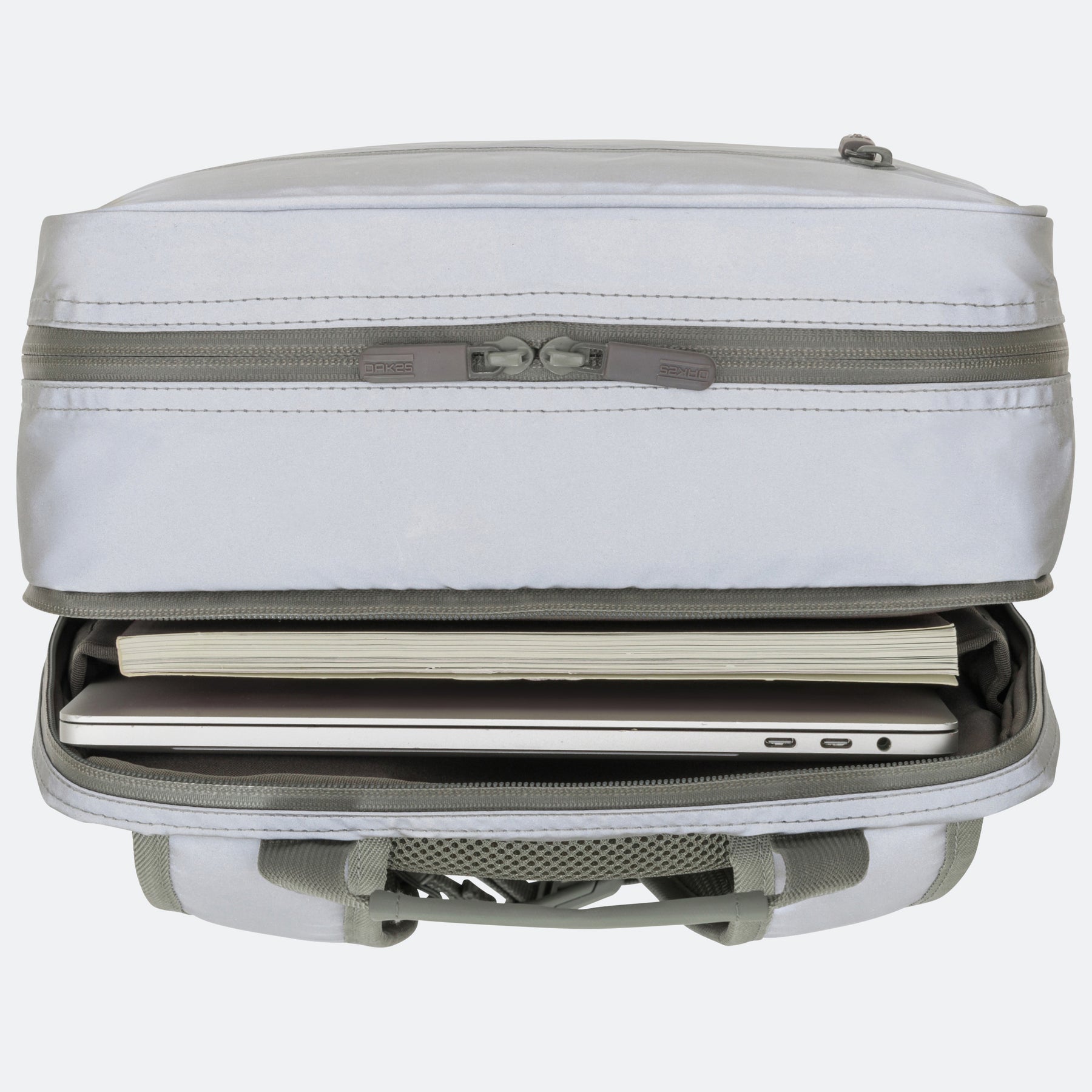 Reflektierender salbeifarbener Rucksack mit geöffnetem Laptopfach und einem Laptop sowie einem Buch darin