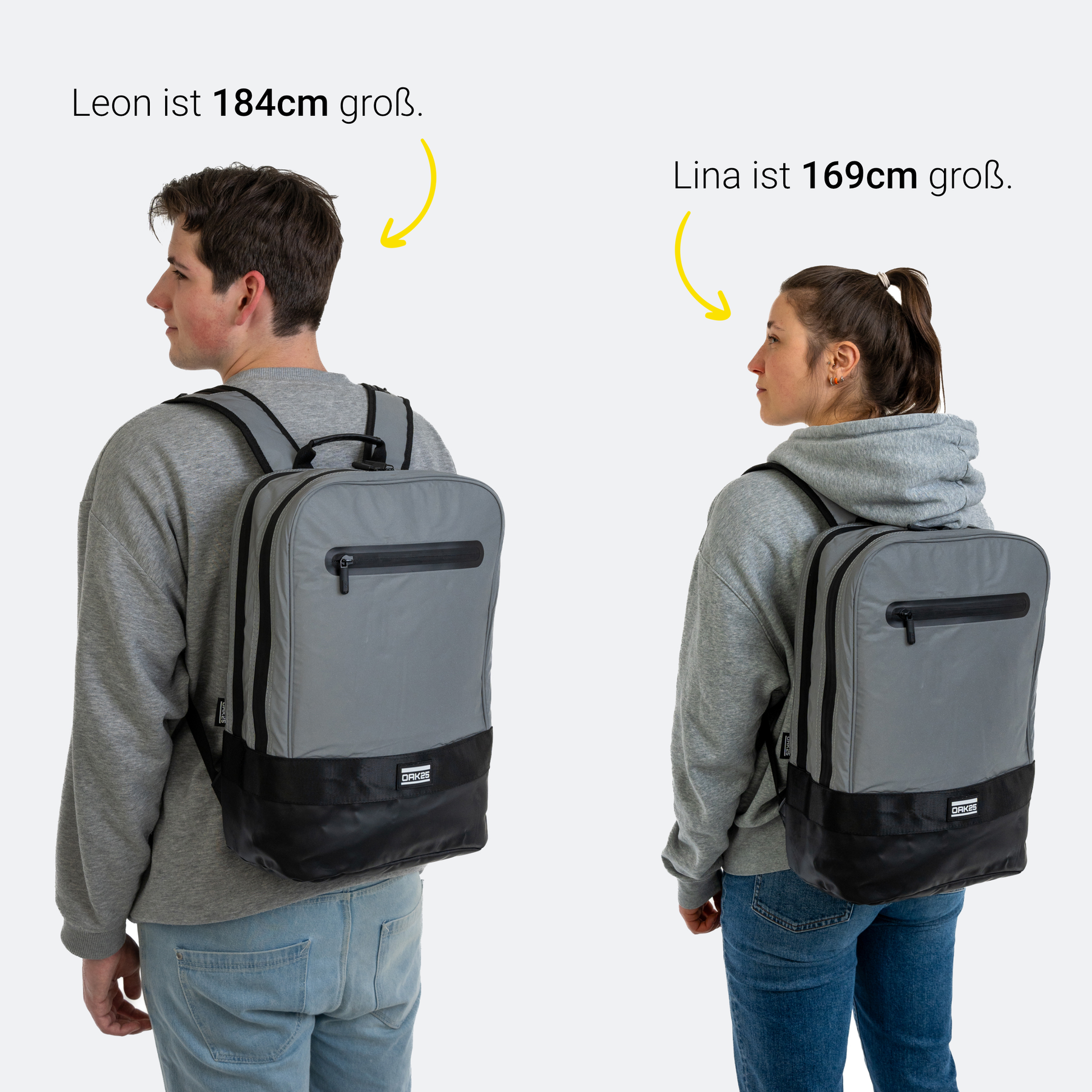 Ein junger Mann (184 cm) und eine junge Frau (169 cm) tragen einen grauen und schwarzen Rucksack von OAK25