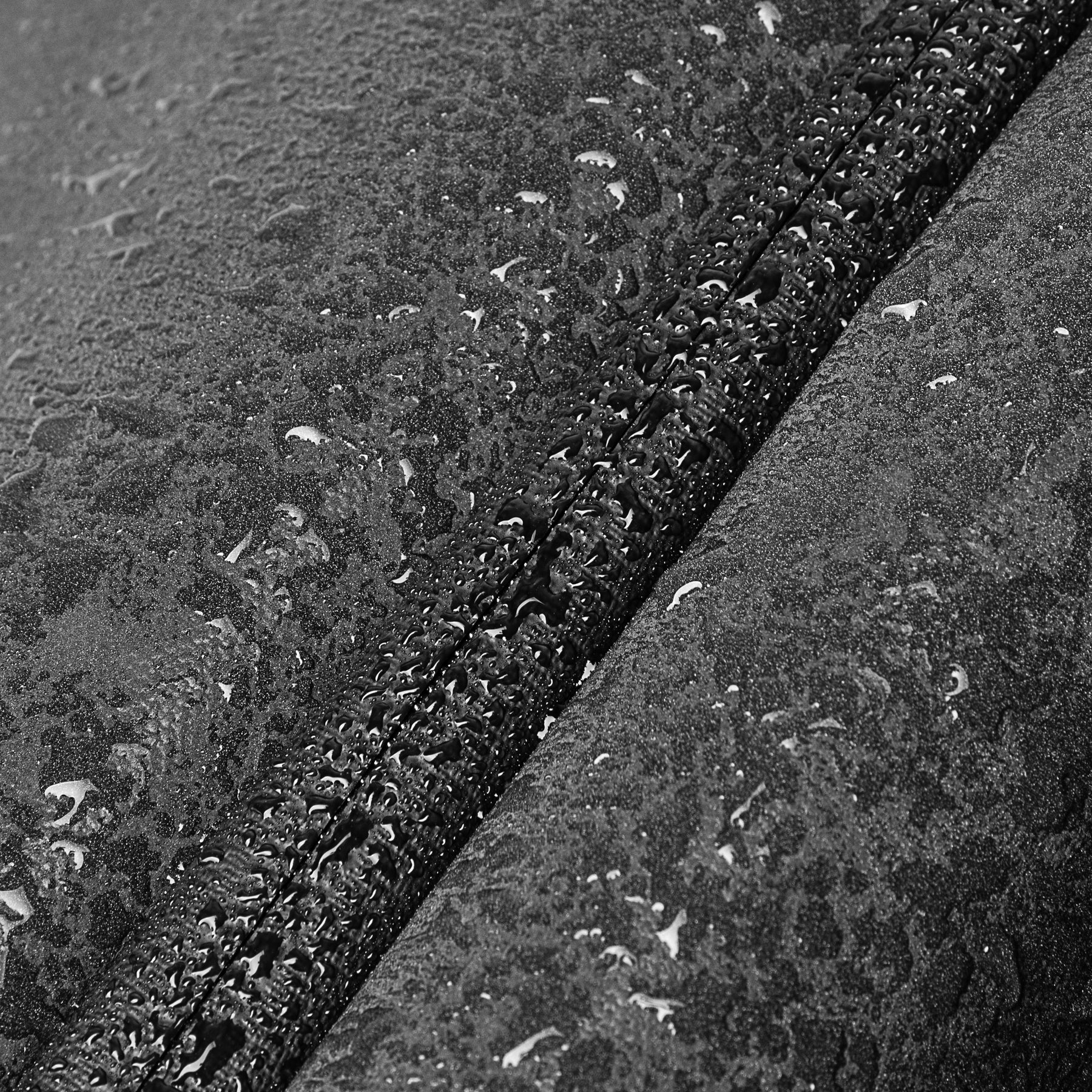 Wasserabweisendes Material mit Wassertropfen auf einer schwarzen Oberfläche, nah an einer Nahtlinie