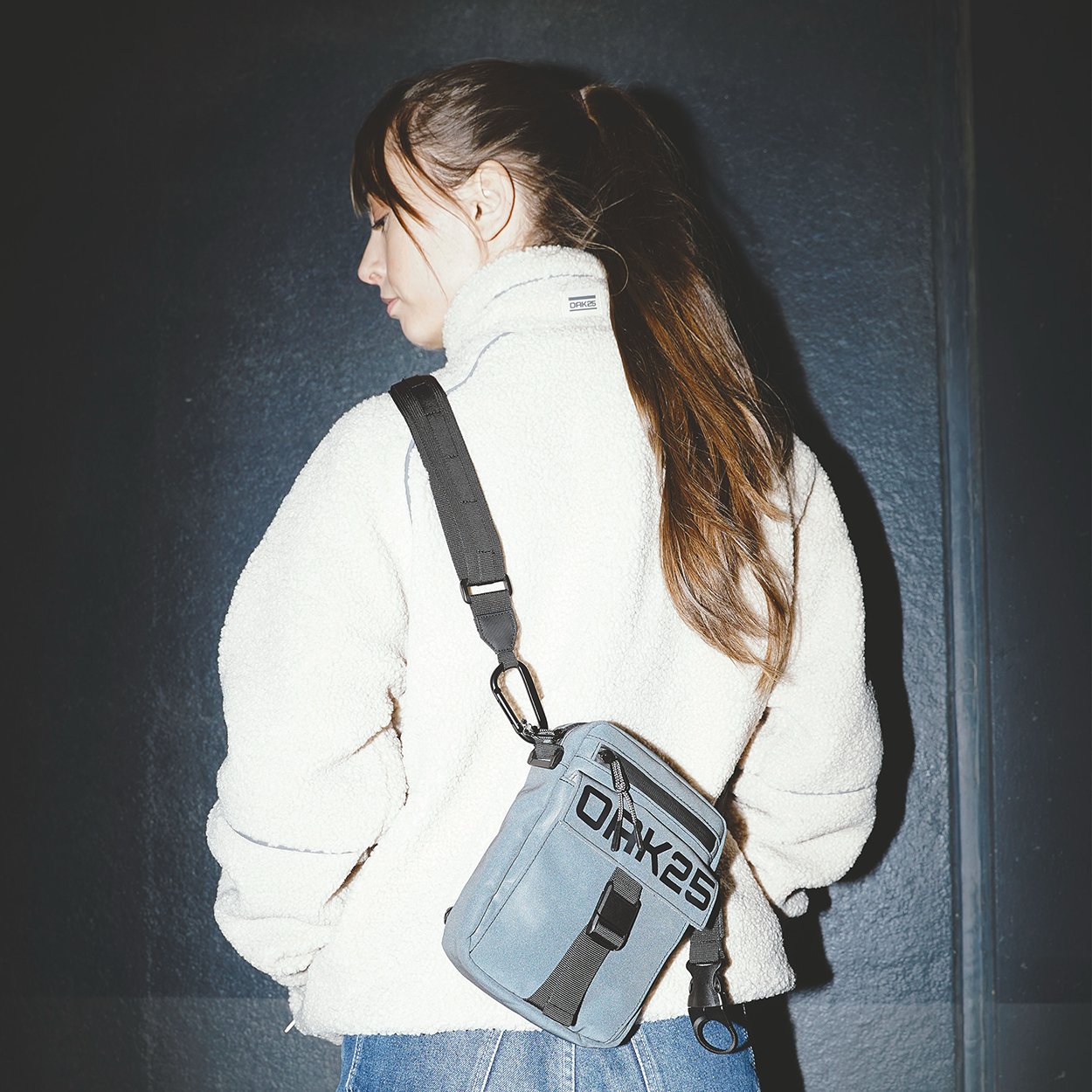 Frau mit langem Zopf und weißer Jacke trägt blau-graue wasserfeste OAK25 Frontpack Bauchtasche über der Schulter