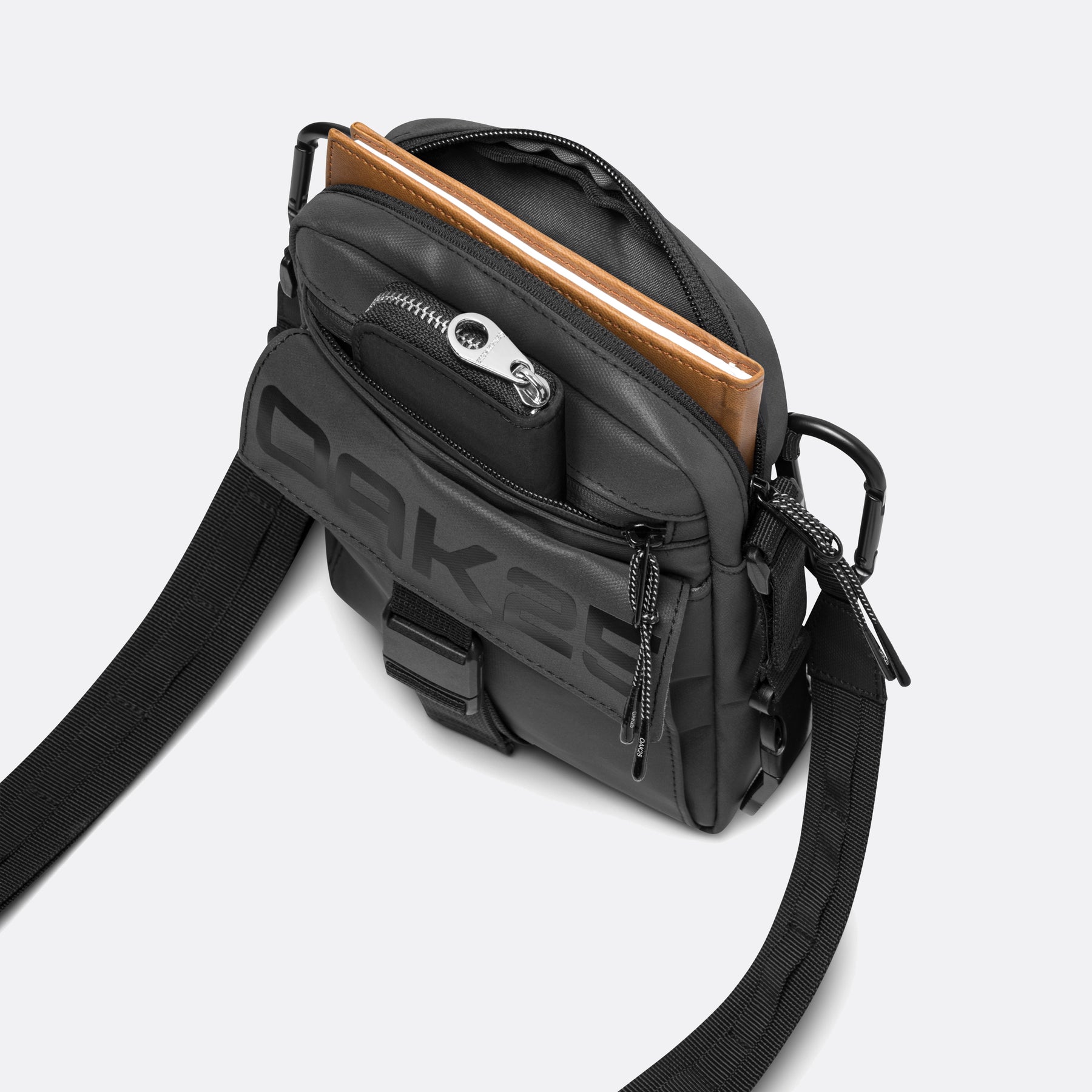 Schwarze OAK25 Luminite Frontpack Umhängetasche mit mehreren Fächern und braunem Notizbuch im Hauptfach