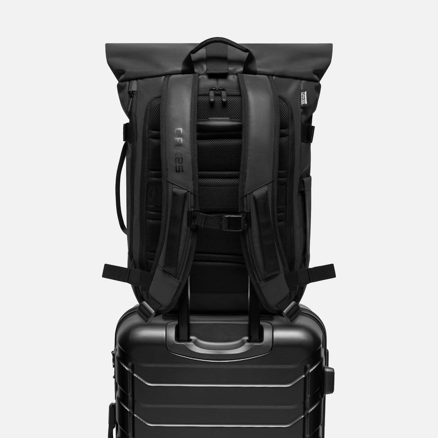 Schwarzer OAK25 Luminite Rolltop-Rucksack mit Gepäckriemen auf schwarzem Hartschalen-Handgepäckkoffer