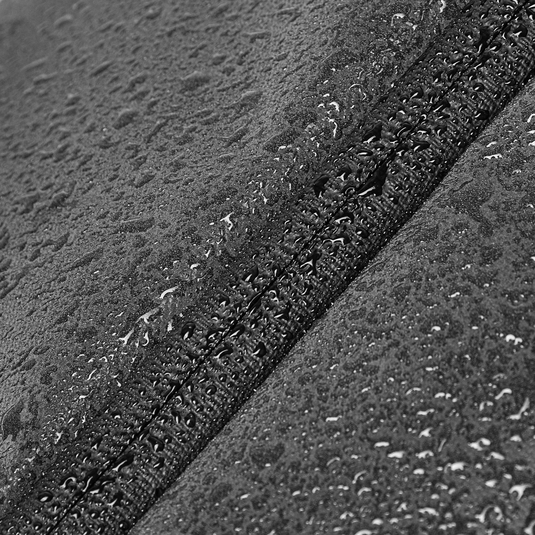 Nahaufnahme eines schwarzen wasserabweisenden Materials mit sichtbaren Wassertropfen und Naht