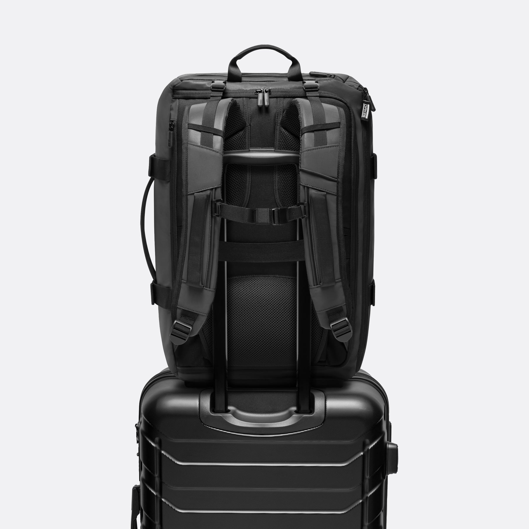 Schwarzer Rucksack mit verstellbaren Trägern, montiert auf schwarzem Hartschalenkoffer mit Teleskopgriff