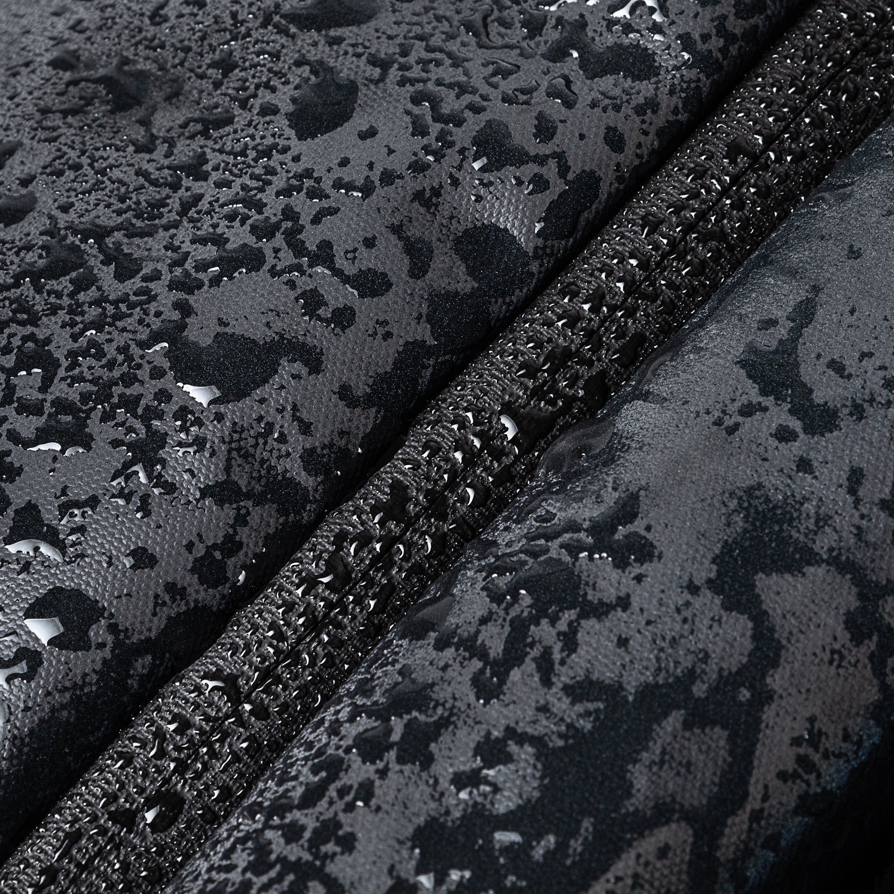 Nahaufnahme eines schwarzen, wasserabweisenden Stoffes mit Regentropfen und einem geschlossenen Reißverschluss