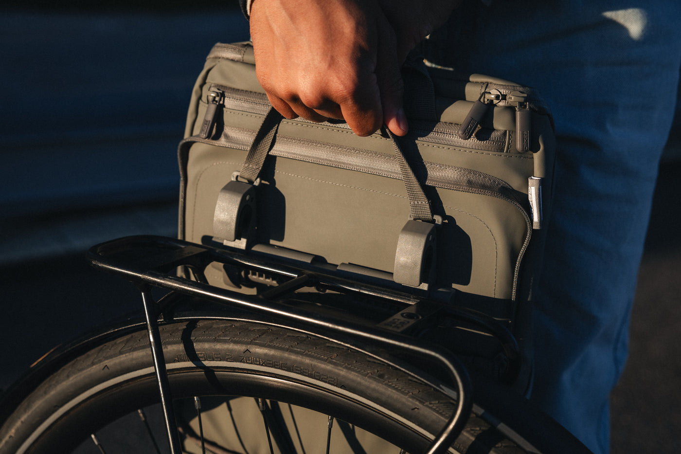 Hand hält graue Tasche mit Schlaufen über Gepäckträger eines Fahrrads