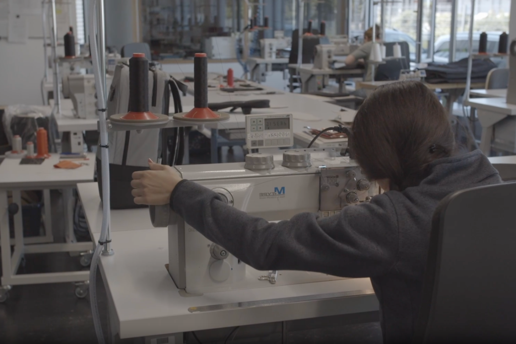 Person bedient industrielle Nähmaschine in Produktionsumgebung mit mehreren Arbeitsplätzen