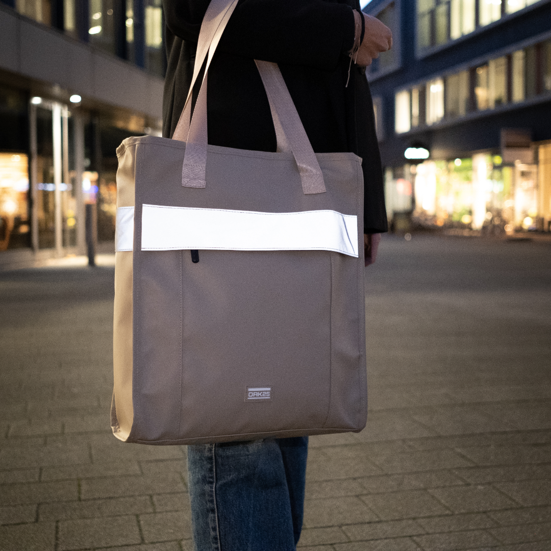 Sandfarbene Tote Bag mit reflektierendem Streifen, getragen von einer Person in der Abendbeleuchtung