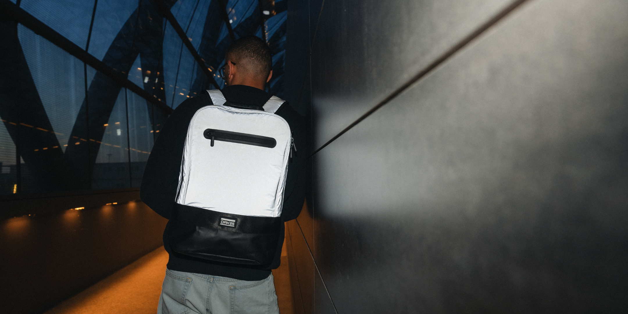 Person mit reflektierendem weißen und schwarzen Rucksack von hinten in einem dunklen, modernen Tunnel