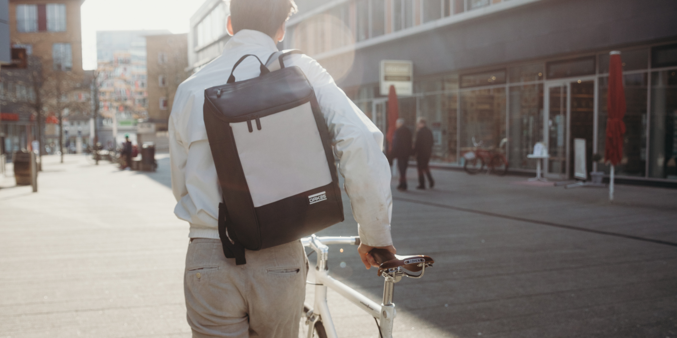 Person mit schwarzem und weißem ORKKA Rucksack hält weißen Fahrradrahmen in einer Stadt