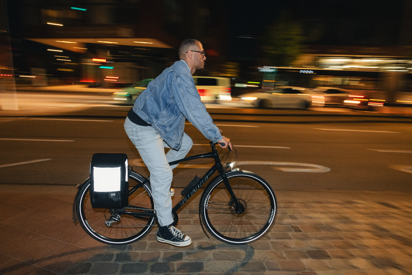 Mann fährt nachts Fahrrad mit reflektierendem schwarzen Fahrradtasche am Gepäckträger